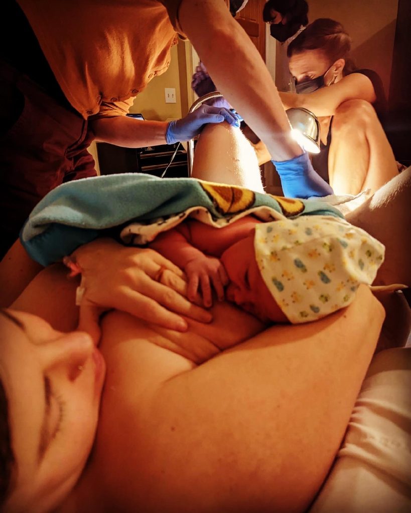 mother holds baby while midwife finishes